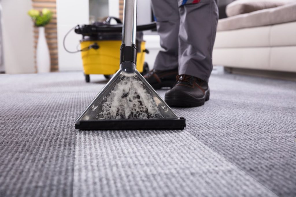 A man using a vacuum cleaner to clean a carpet in a well-lit room, focusing on removing dirt and debris.