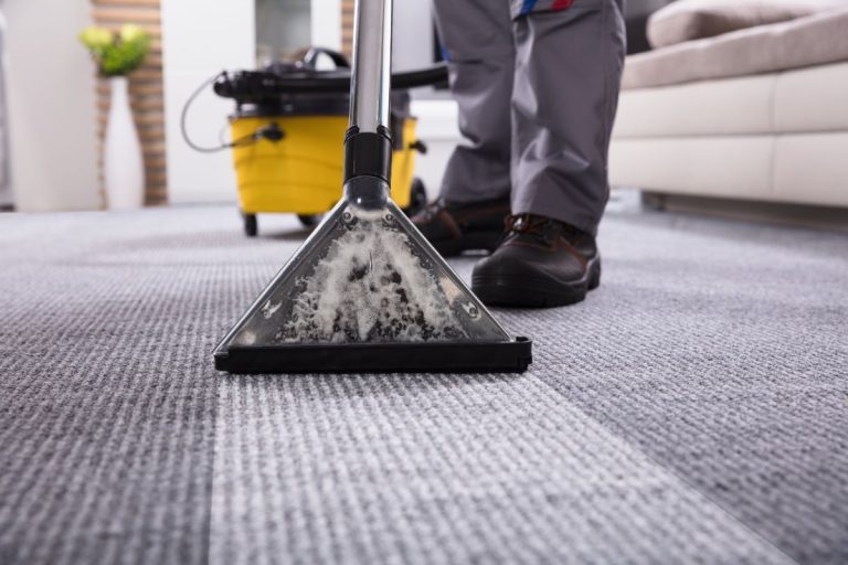 A man using a vacuum cleaner to clean a carpet in a well-lit room, focusing on removing dirt and debris.