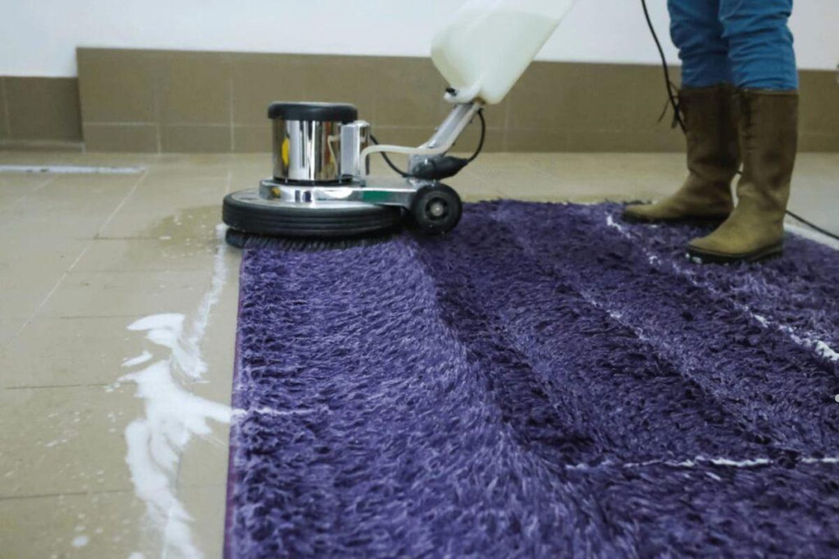 A person vacuums a purple rug, focusing on removing dirt and debris from its textured surface.