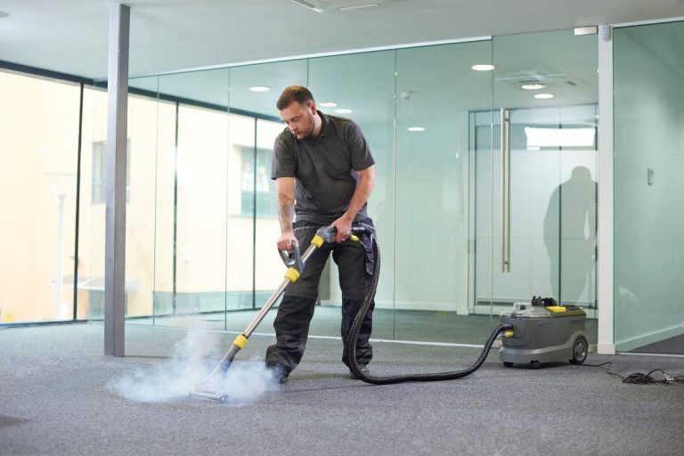 A man using a vacuum cleaner to clean a carpet in a well-lit room, focusing on removing dirt and debris.